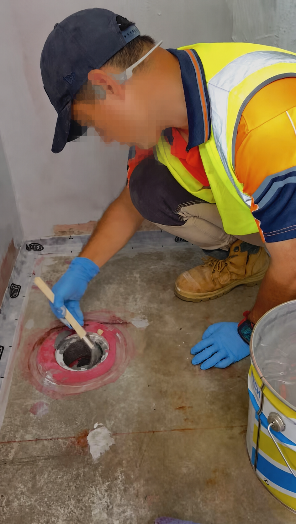 Worker preparing a wet-area drain before waterproofing, with face obscured for privacy